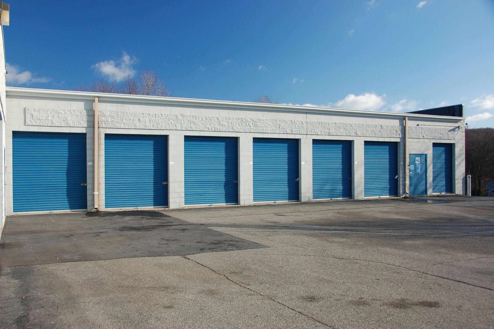 Row of blue storage unit doors on a concrete lot, under a blue sky.