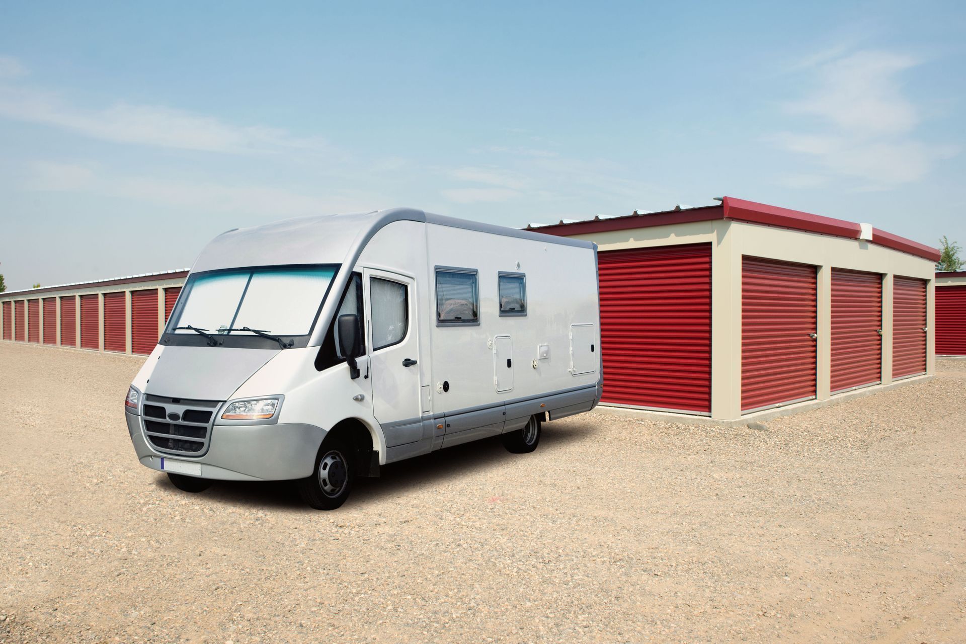 White van parked near red storage units on gravel under a blue sky.