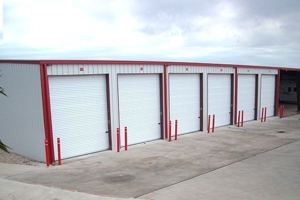 Storage units with white doors and red trim under cloudy sky.