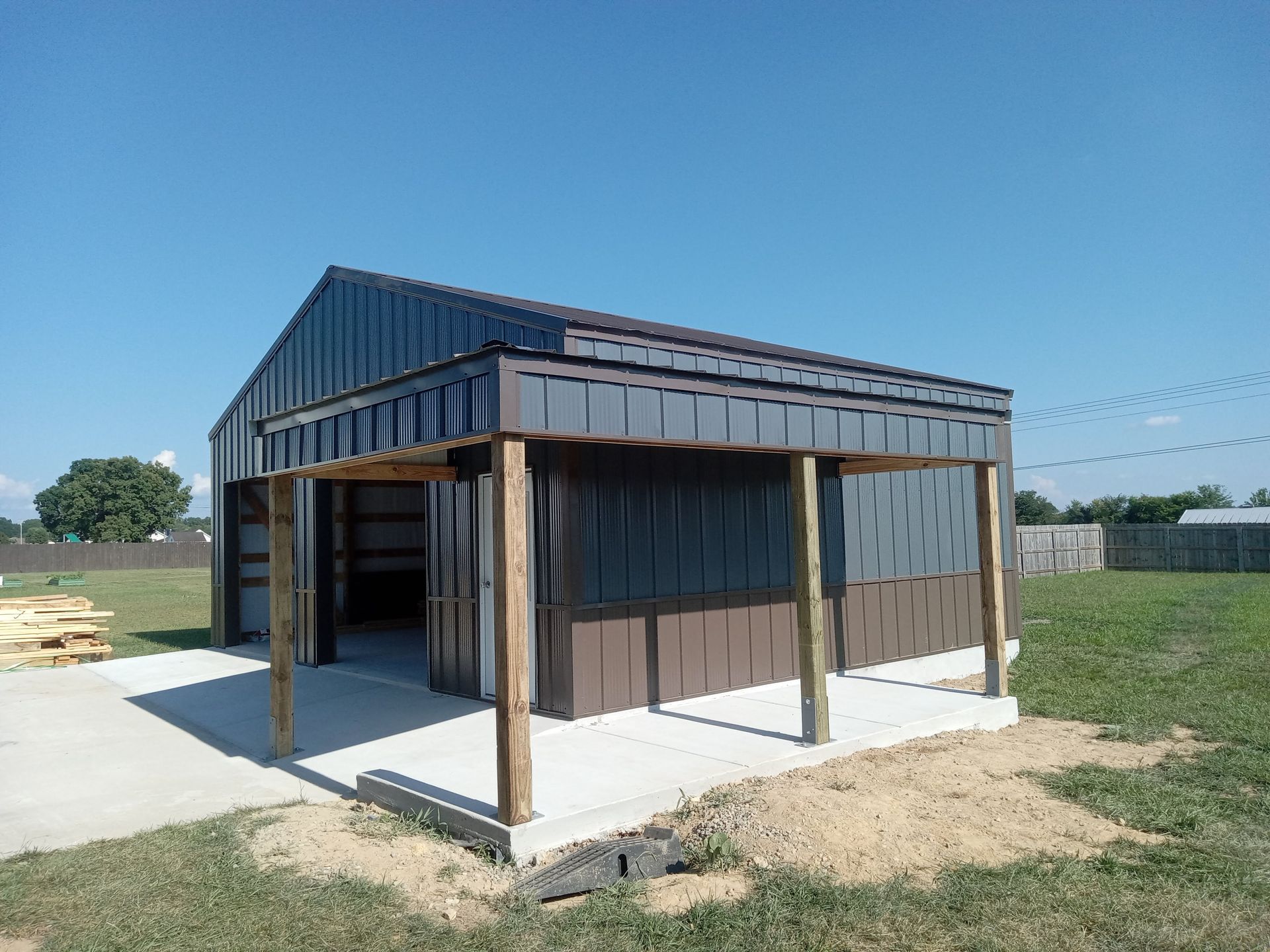 A shed with a porch is sitting in the middle of a grassy field.