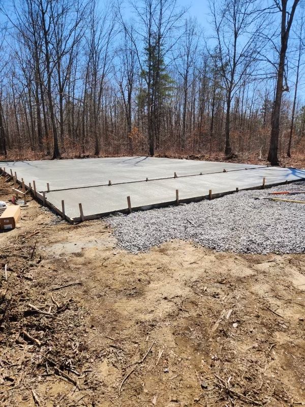 A large concrete slab is sitting in the middle of a dirt field surrounded by trees.