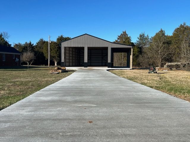 A concrete driveway leading to a garage in the middle of a field.