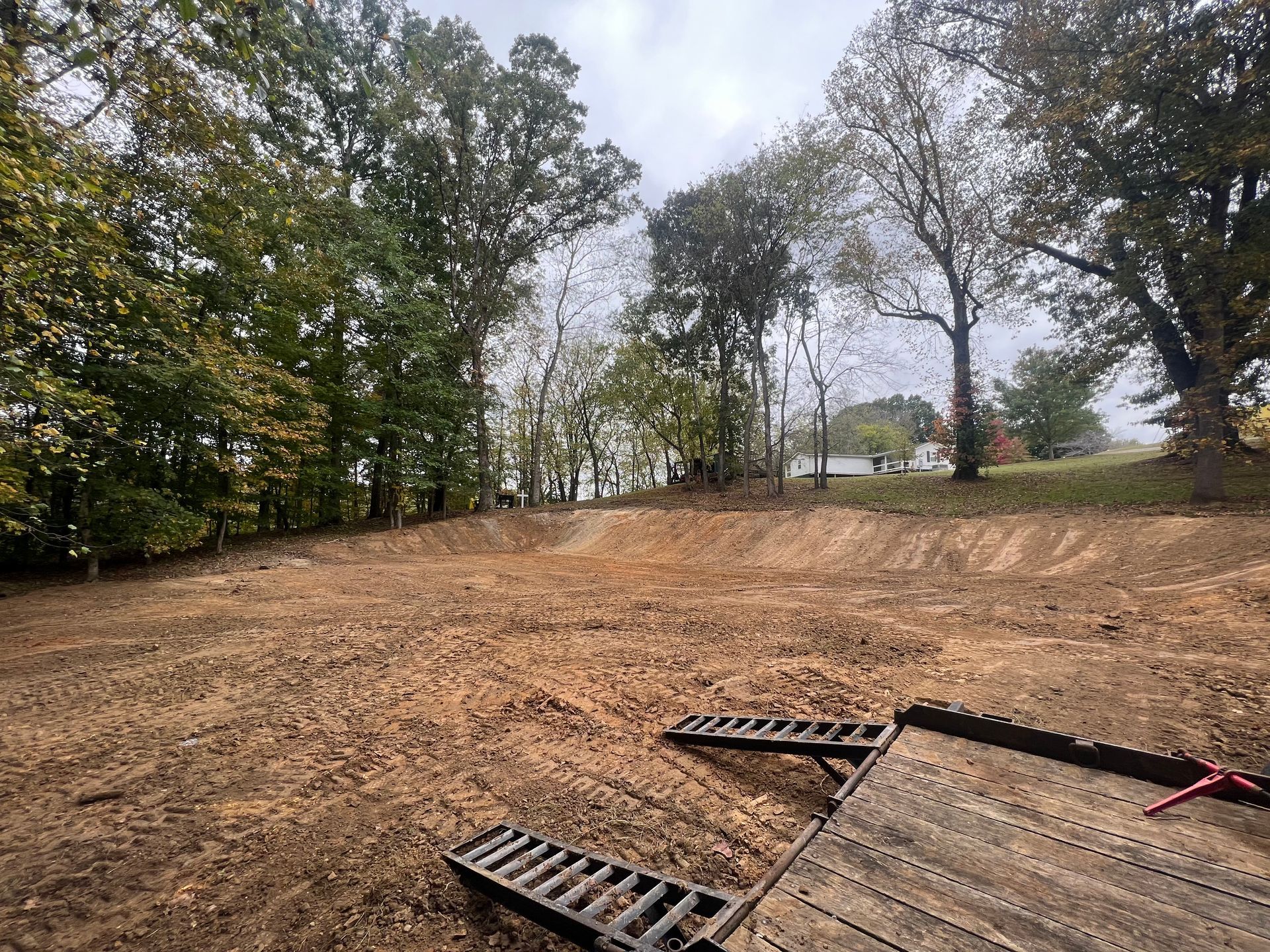 A large dirt field with trees in the background and a trailer in the foreground.