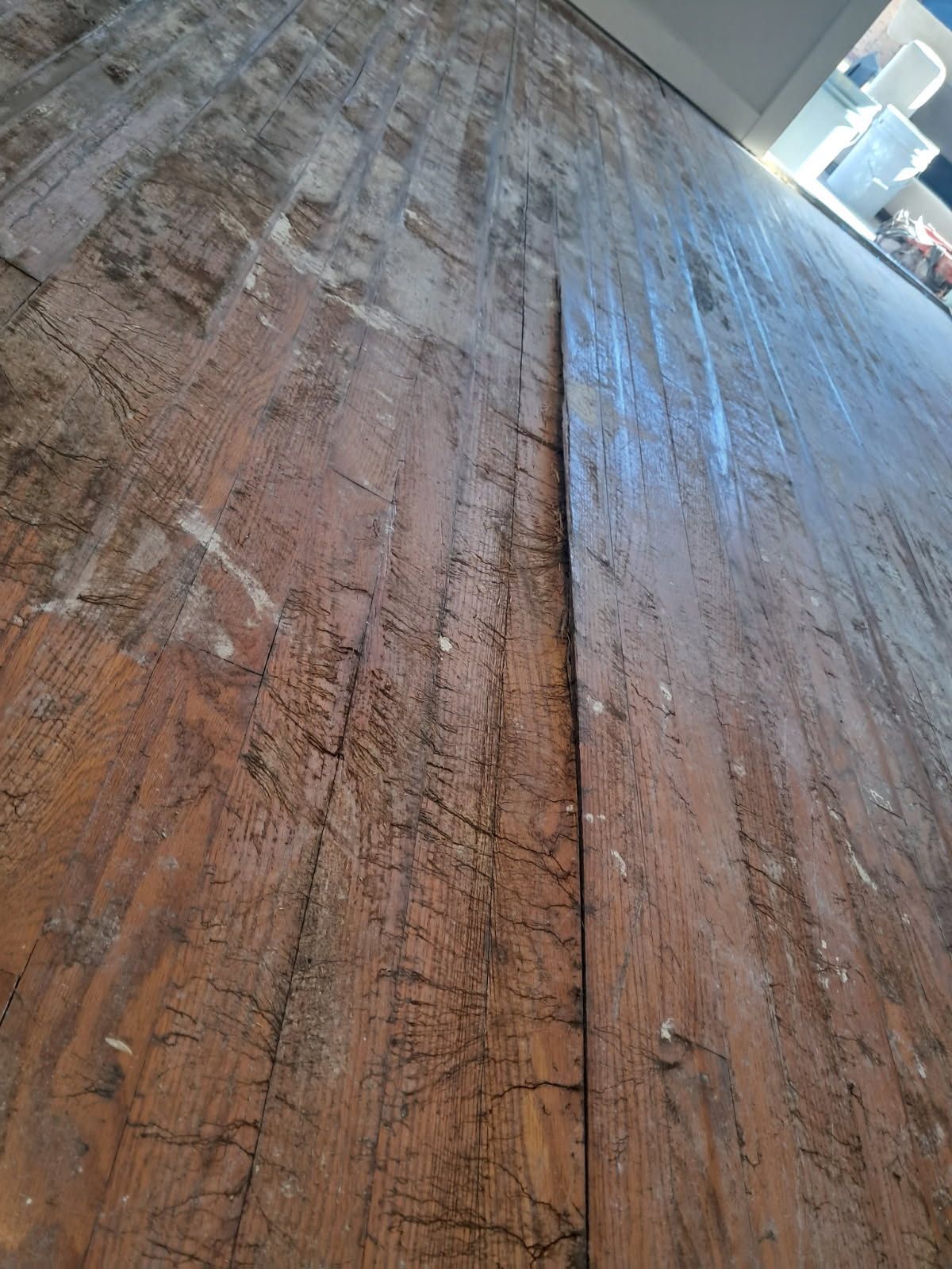 Close up of weathered, dark brown wooden floorboards with a wide crack down the center.