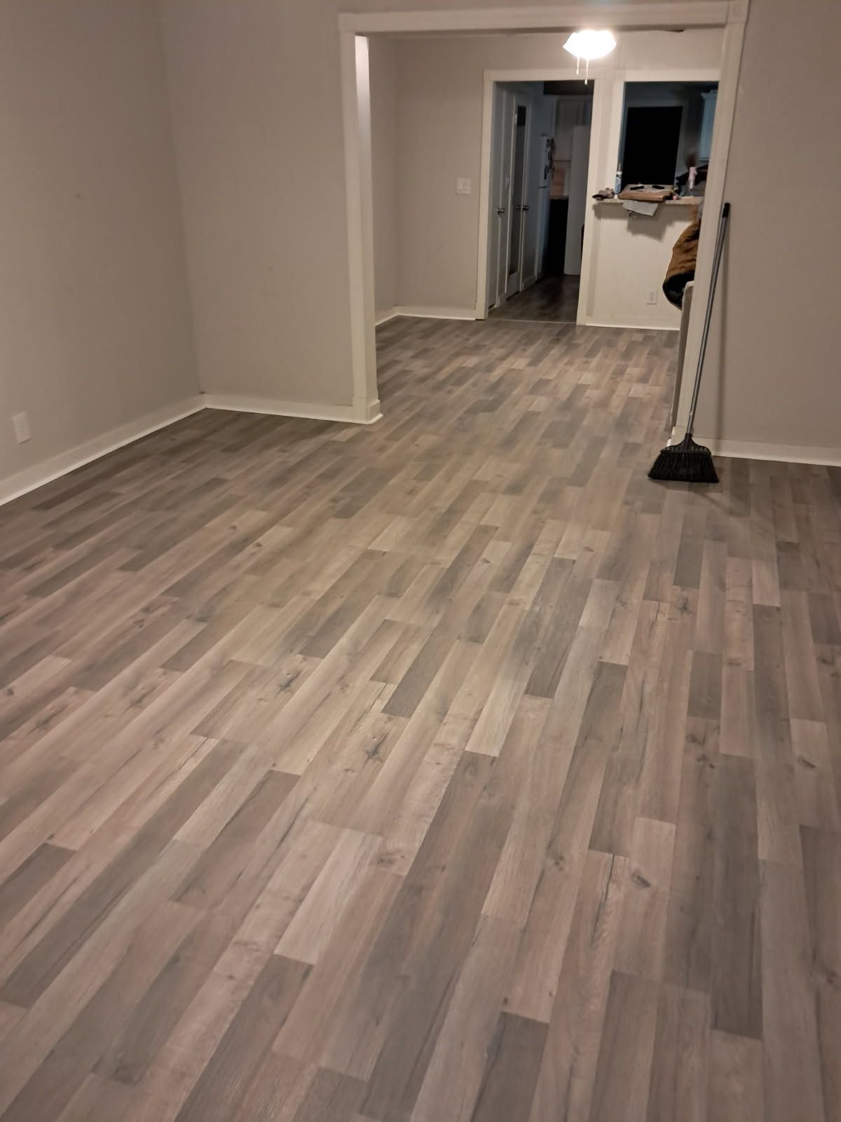 Light gray wood look flooring extends into an open doorway of a room with white walls and trim.