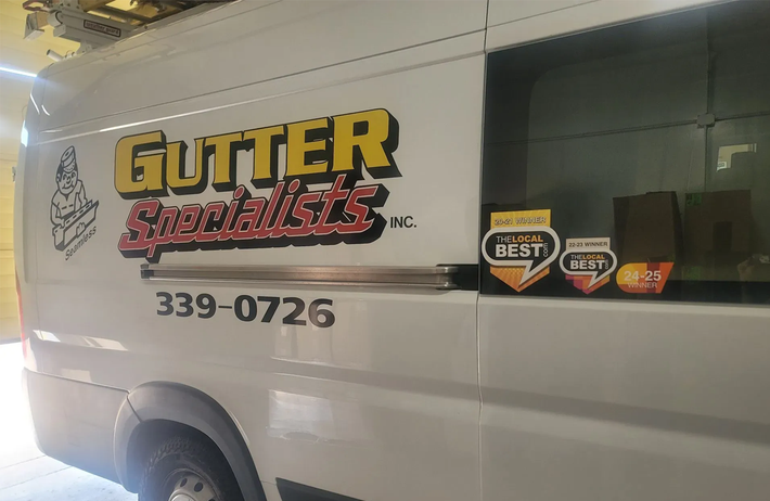 A white van with gutter specialists written on the side is parked in a garage.