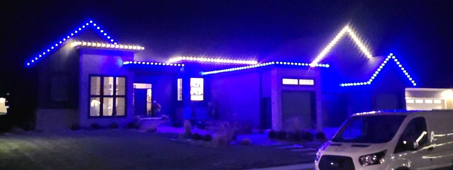 A white van is parked in front of a house with blue lights on it.