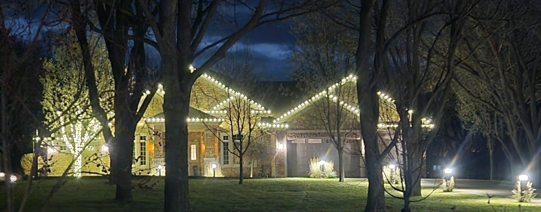 A house with christmas lights on the roof is surrounded by trees at night.