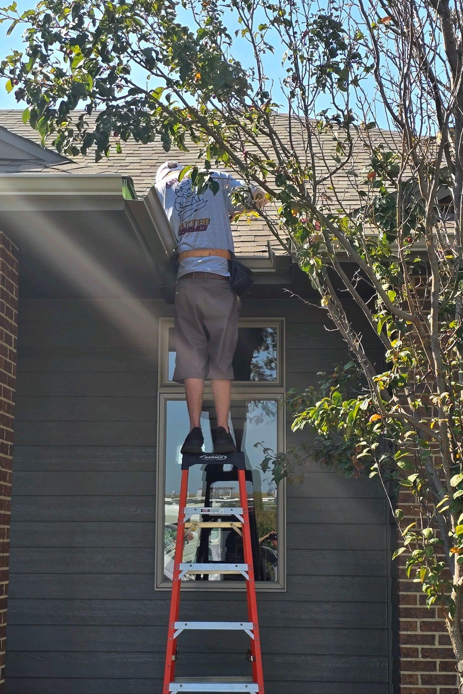 A man is standing on a ladder working on the roof of a house.
