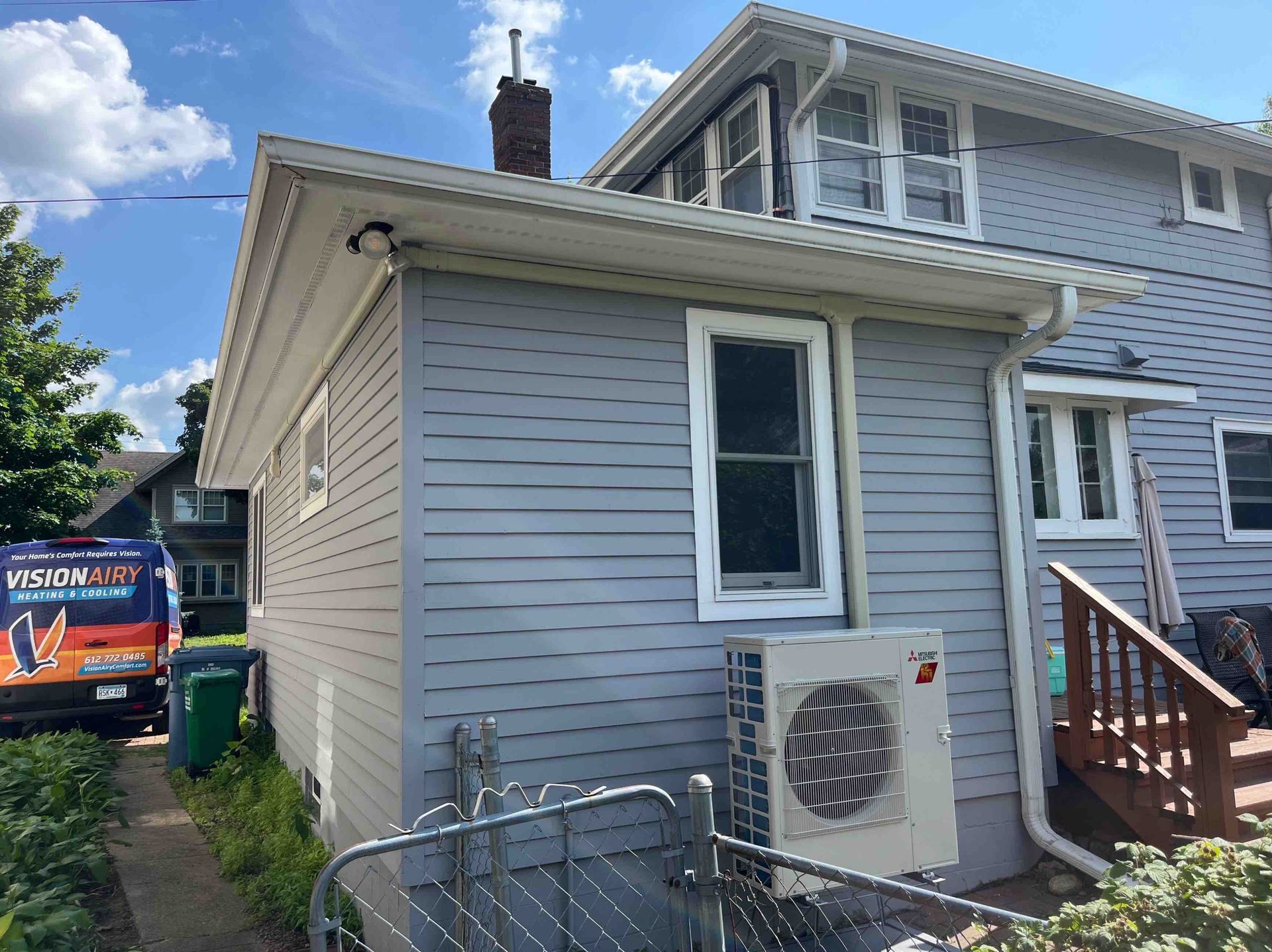 Gray house with white trim, gutters, and an air conditioner; blue sky in the background.