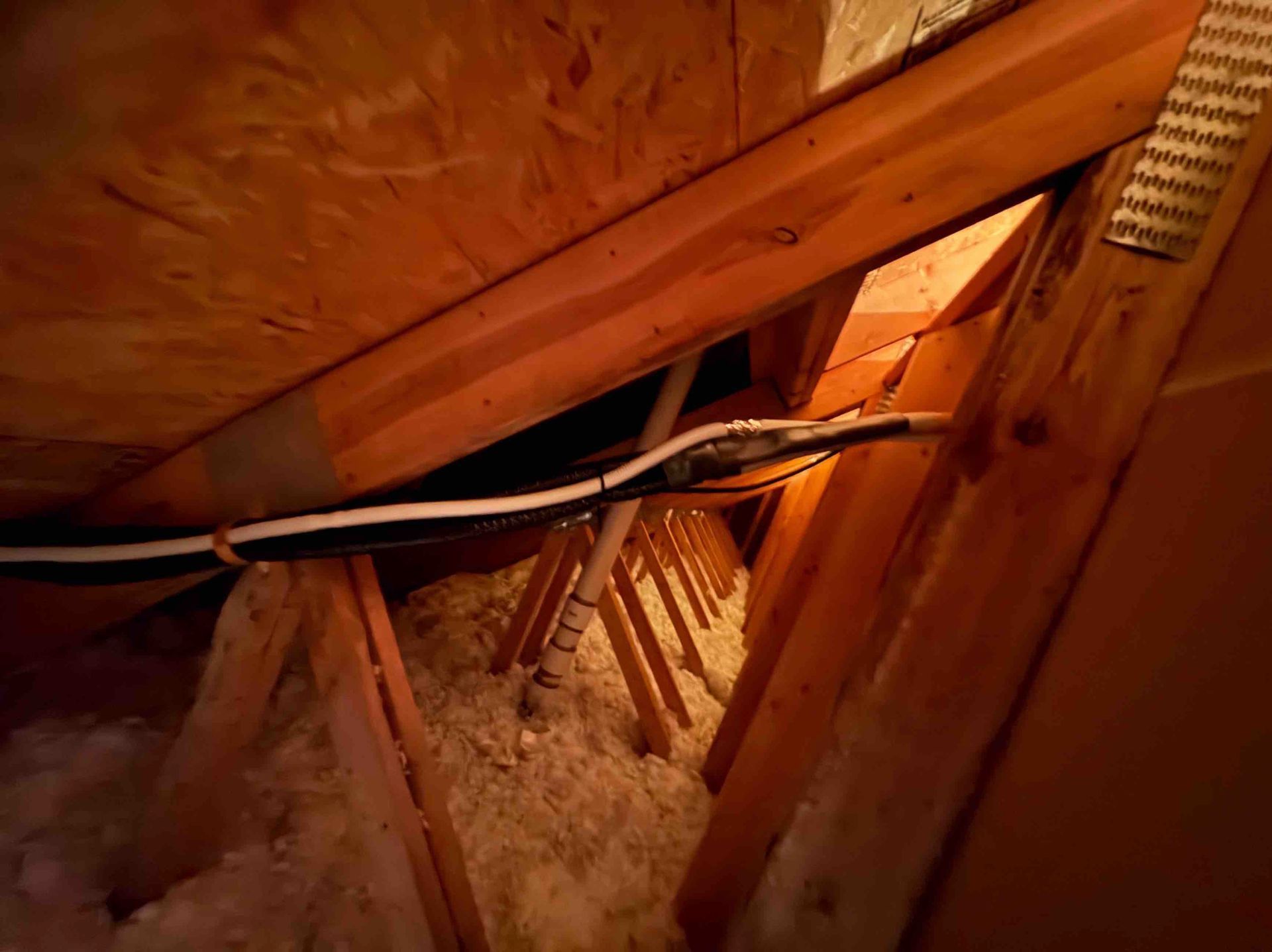 Attic with wooden beams, insulation, and electrical wiring running along the structure.