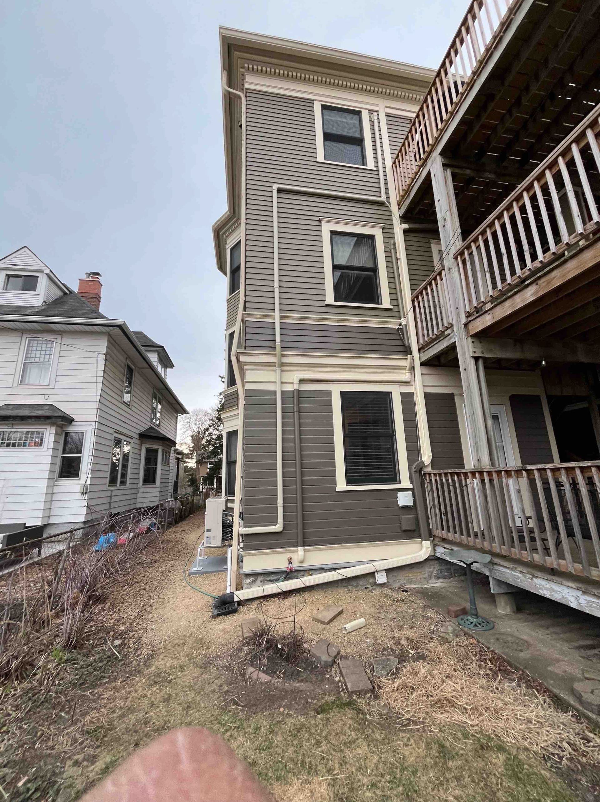 Multi-story brown building with side stairs and adjacent white house on a cloudy day.