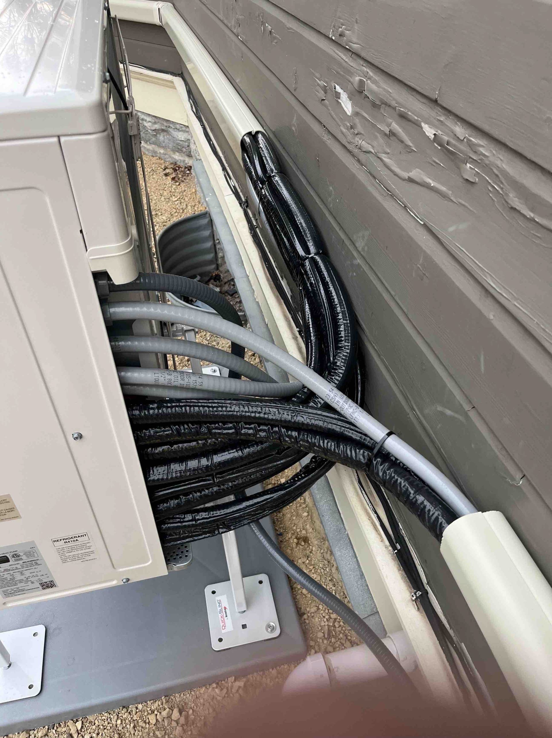 Air conditioner unit with multiple black and gray insulated cables running along a beige wall.