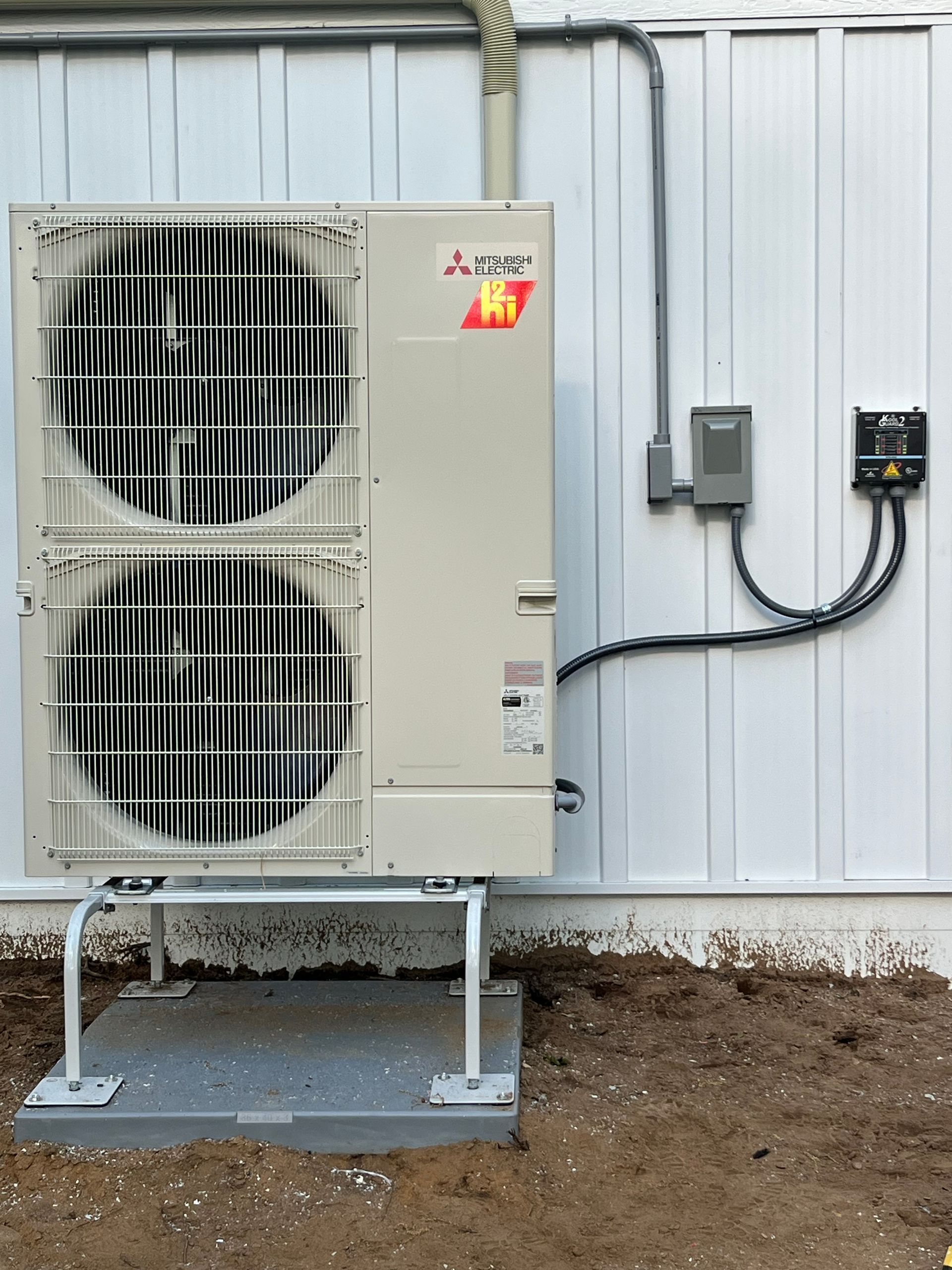 Mitsubishi heat pump unit mounted on a concrete pad, with electrical conduit and wiring.