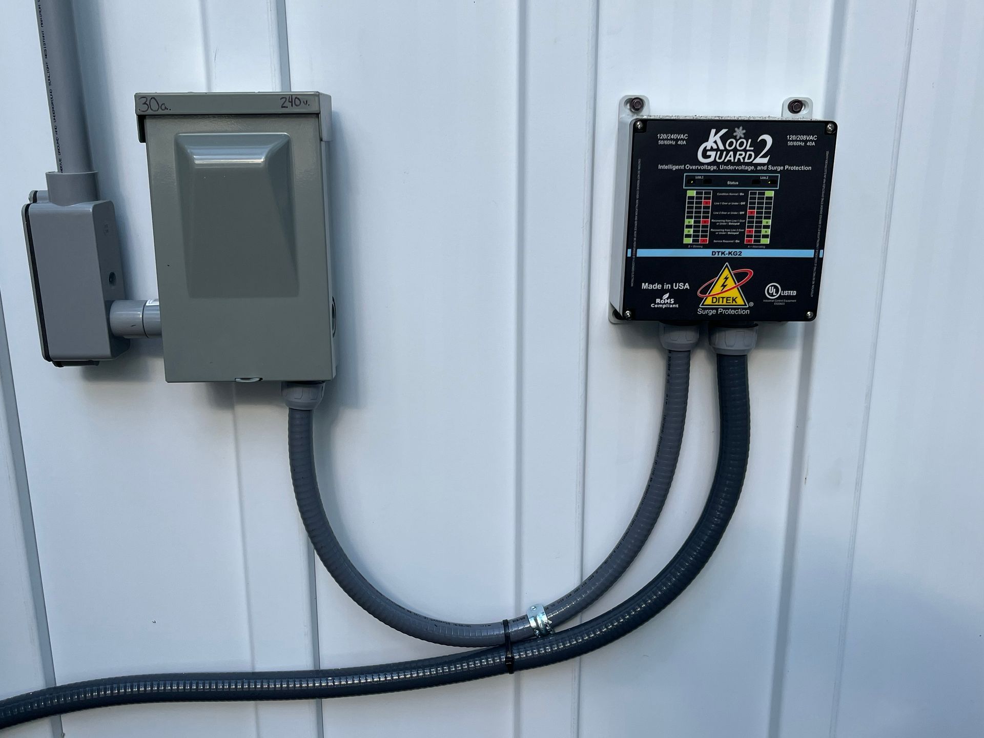 Electrical box and charger mounted on a white wall, connected by gray conduit.