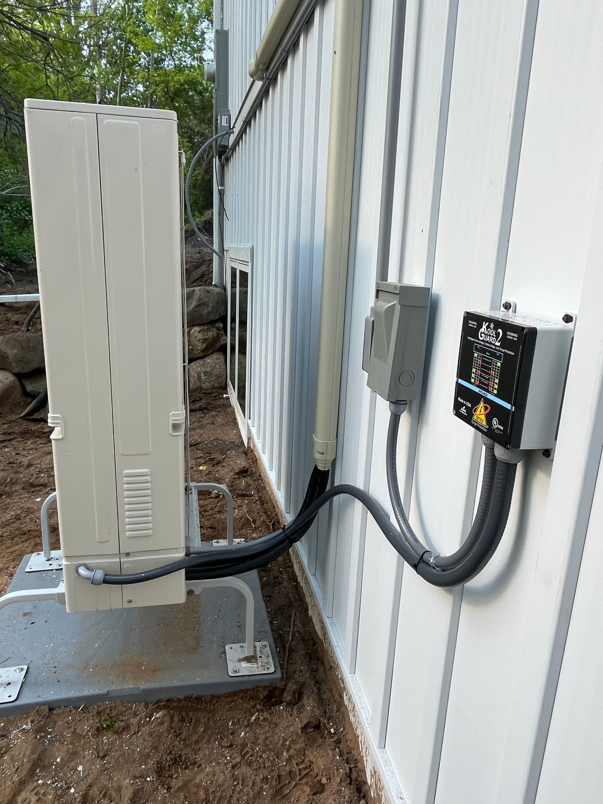 Outdoor electrical equipment mounted on a white building: inverter, junction box, conduit, and AC unit.