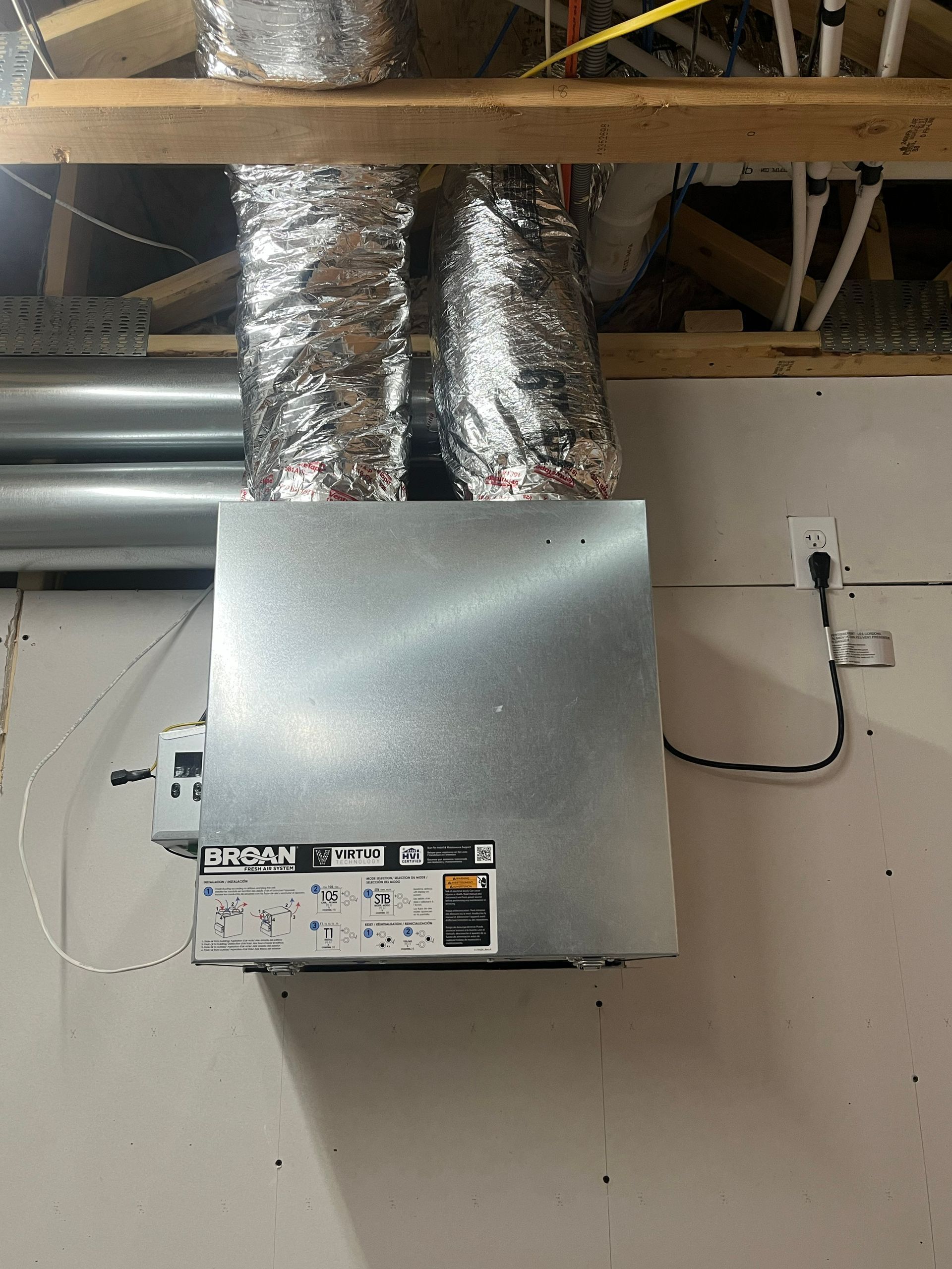 HVAC air handler unit attached to ductwork in a basement ceiling, with a nearby electrical outlet.