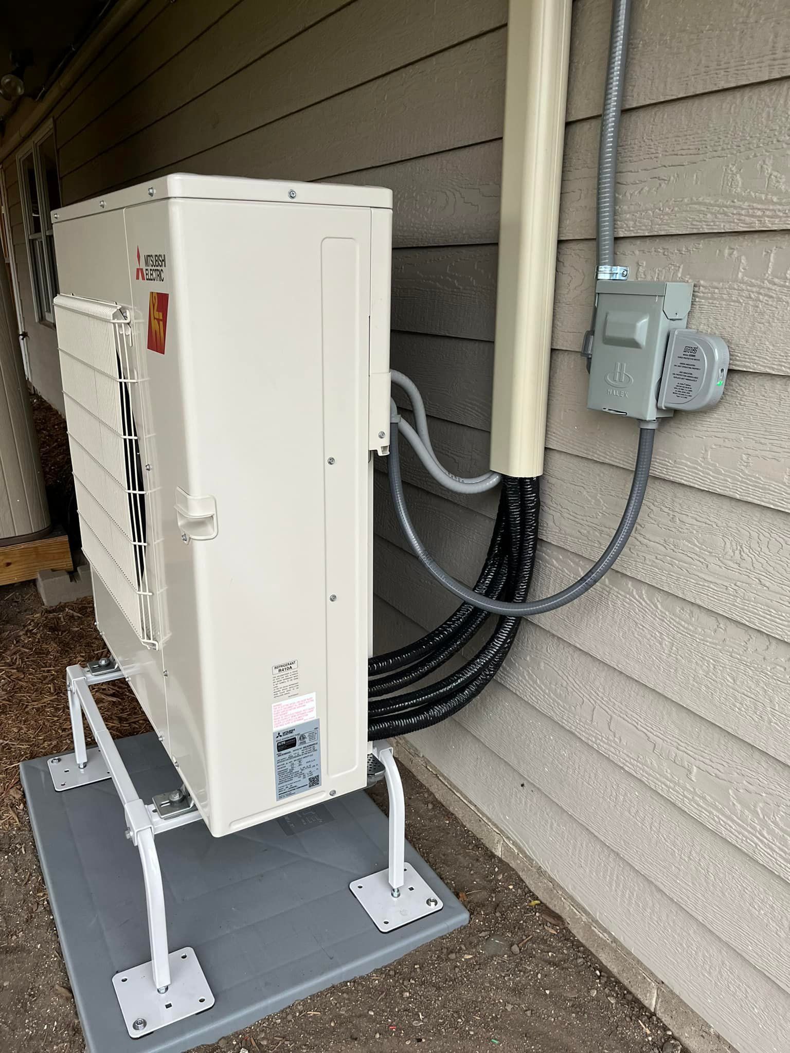 Air conditioner unit mounted on a platform against a building with electrical conduit and junction box.