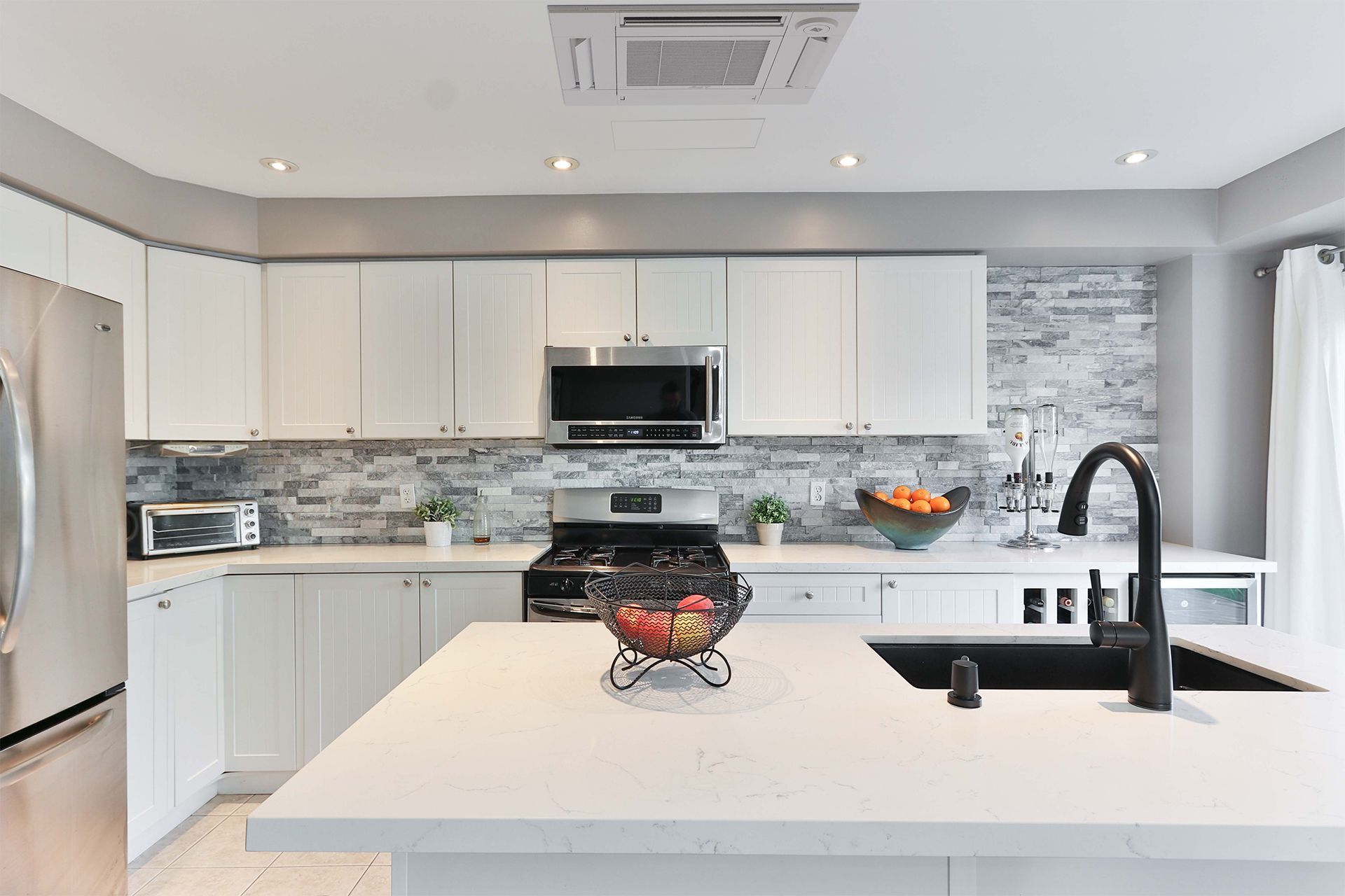 Modern white kitchen with island, stainless steel appliances, and gray backsplash.