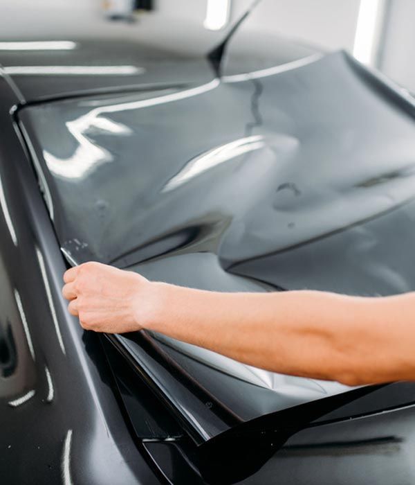Person applying tint to a car window with a tool, in a garage.