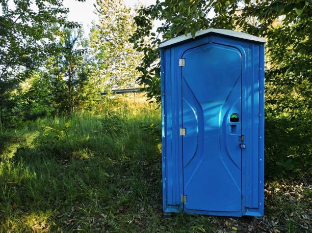 A blue portable toilet is sitting in the middle of a grassy field.