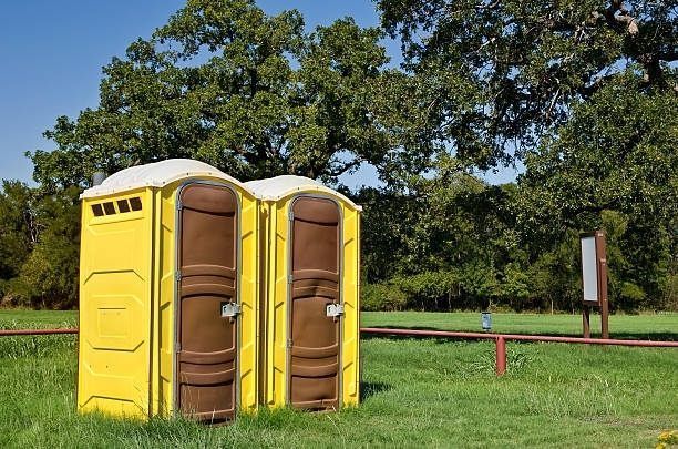 Three yellow and brown portable toilets are sitting in a grassy field.