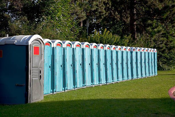 A row of portable toilets are lined up in a grassy field.