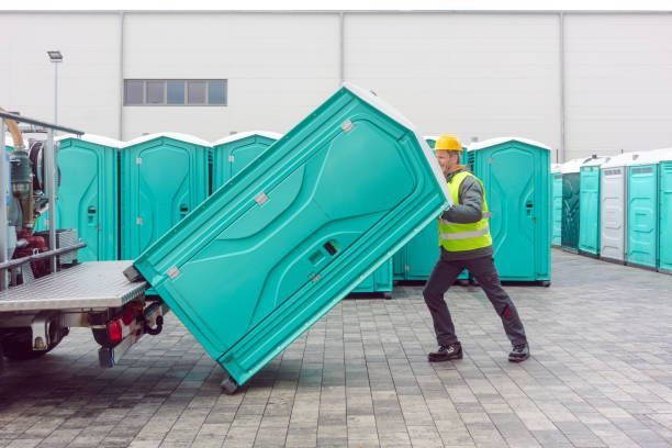 A man is carrying a portable toilet out of a truck.