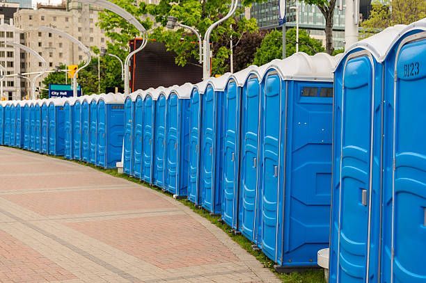 A row of blue portable toilets are lined up on a sidewalk.