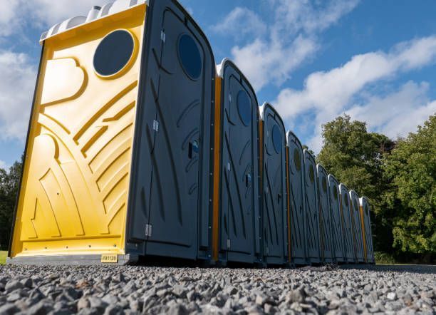 A row of portable toilets are lined up on gravel.