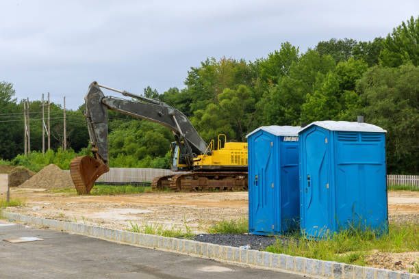 A construction site with two blue portable toilets and a yellow excavator.