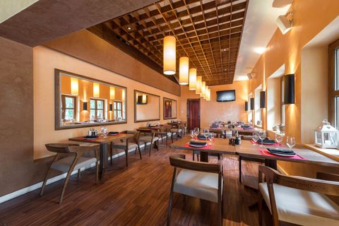 Restaurant interior with wood tables, chairs, and floors. Warm colors, decorative mirrors and hanging lights.