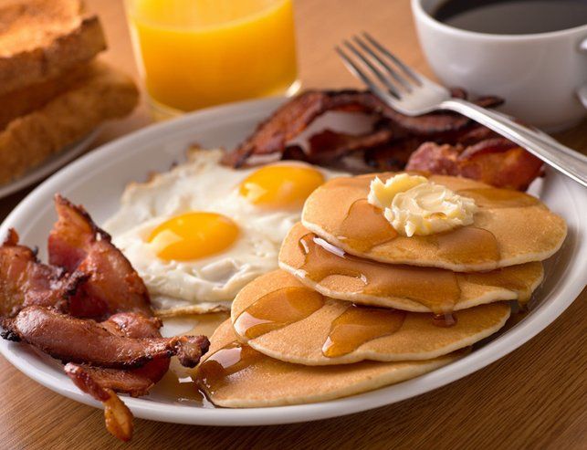 A white plate topped with pancakes eggs bacon and syrup