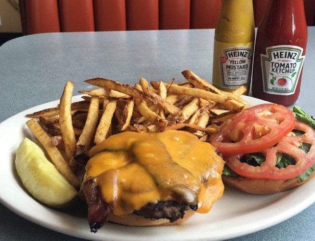 A hamburger and french fries on a plate with heinz ketchup in the background