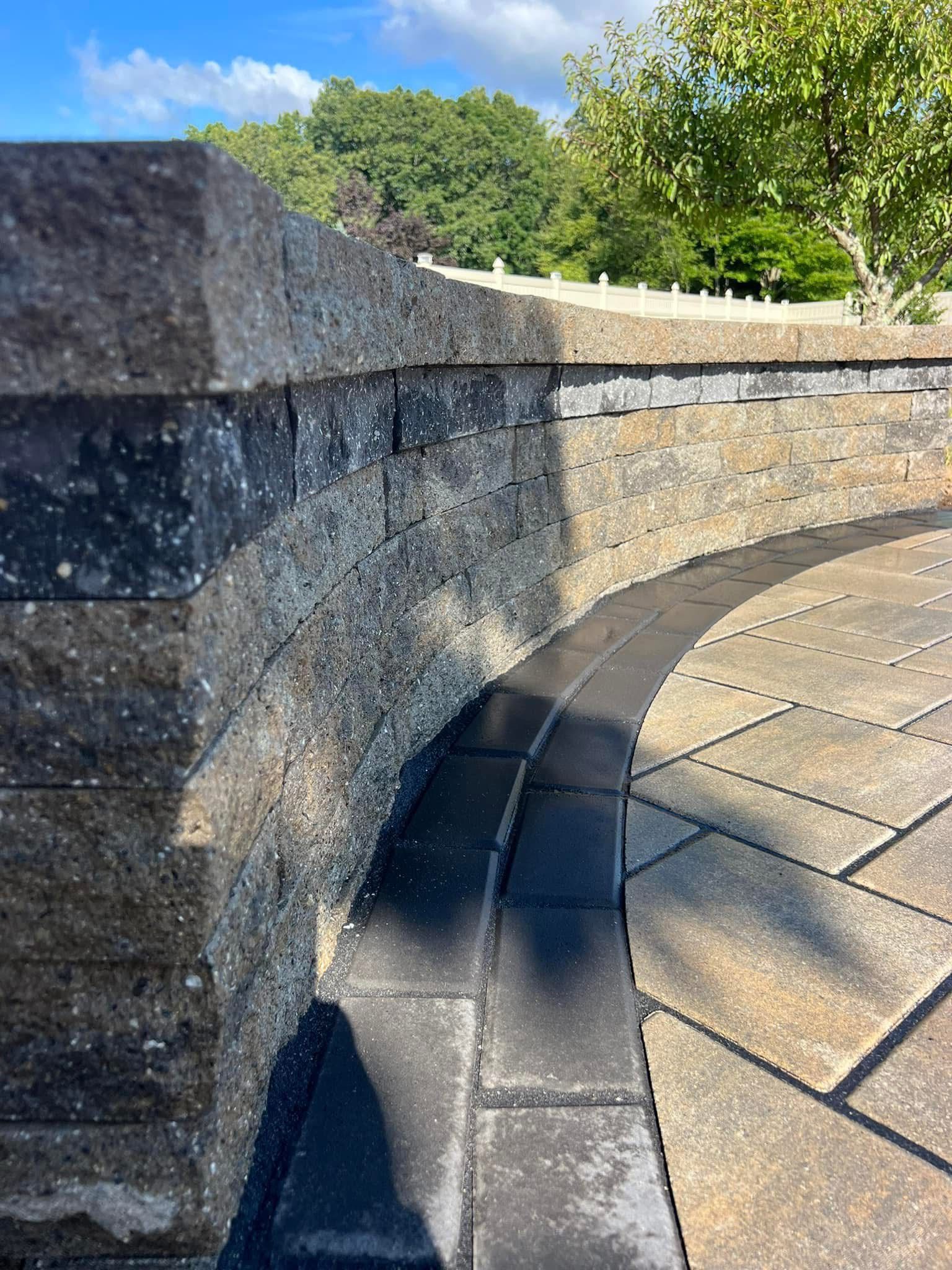 A stone wall with a curved patio in front of it.