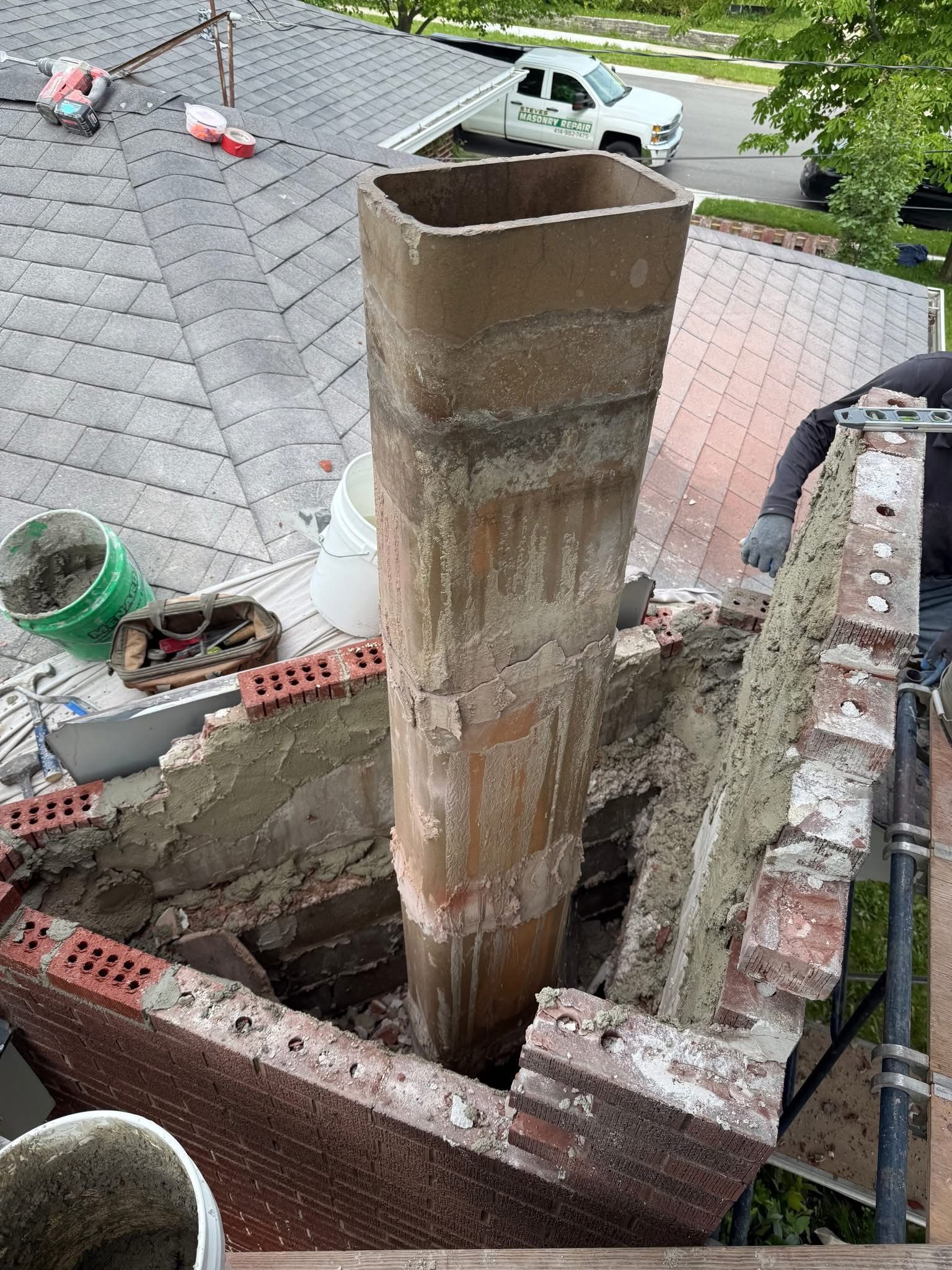 A man is working on a chimney on the roof of a house.