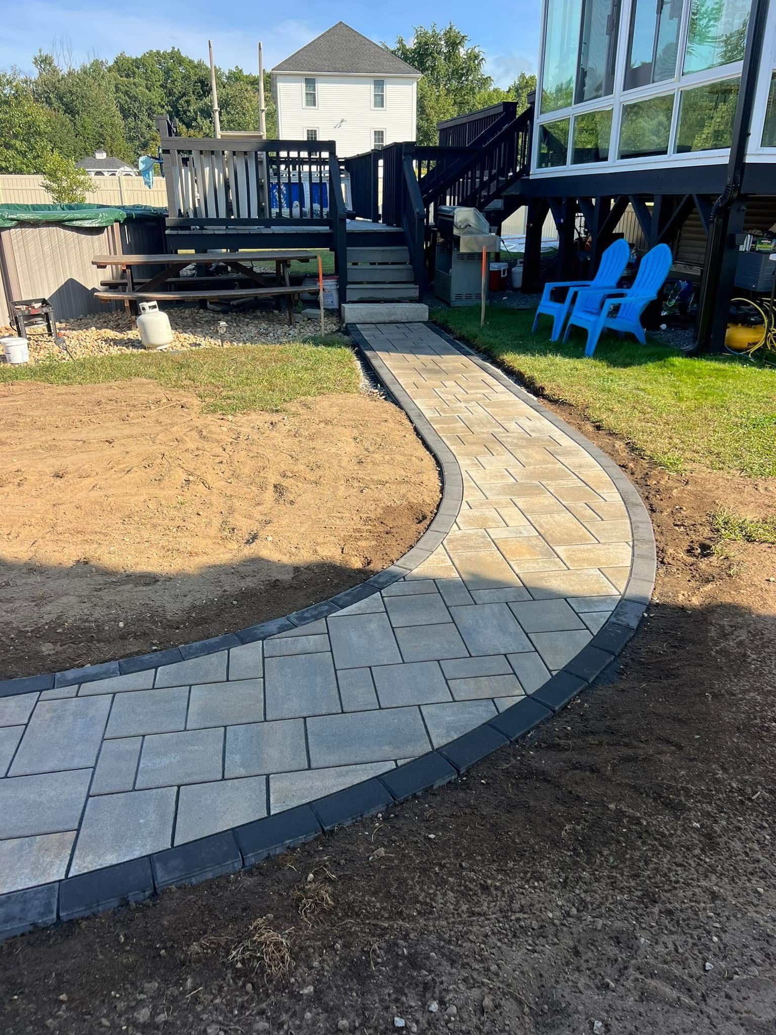 A walkway leading to a house with a deck and blue chairs.