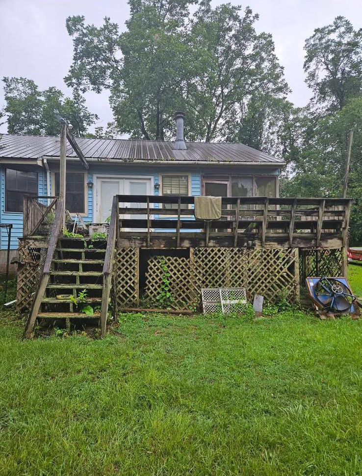 A house with a deck and stairs is sitting on top of a lush green field.