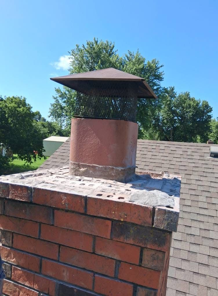 A brick chimney on top of a roof with trees in the background.