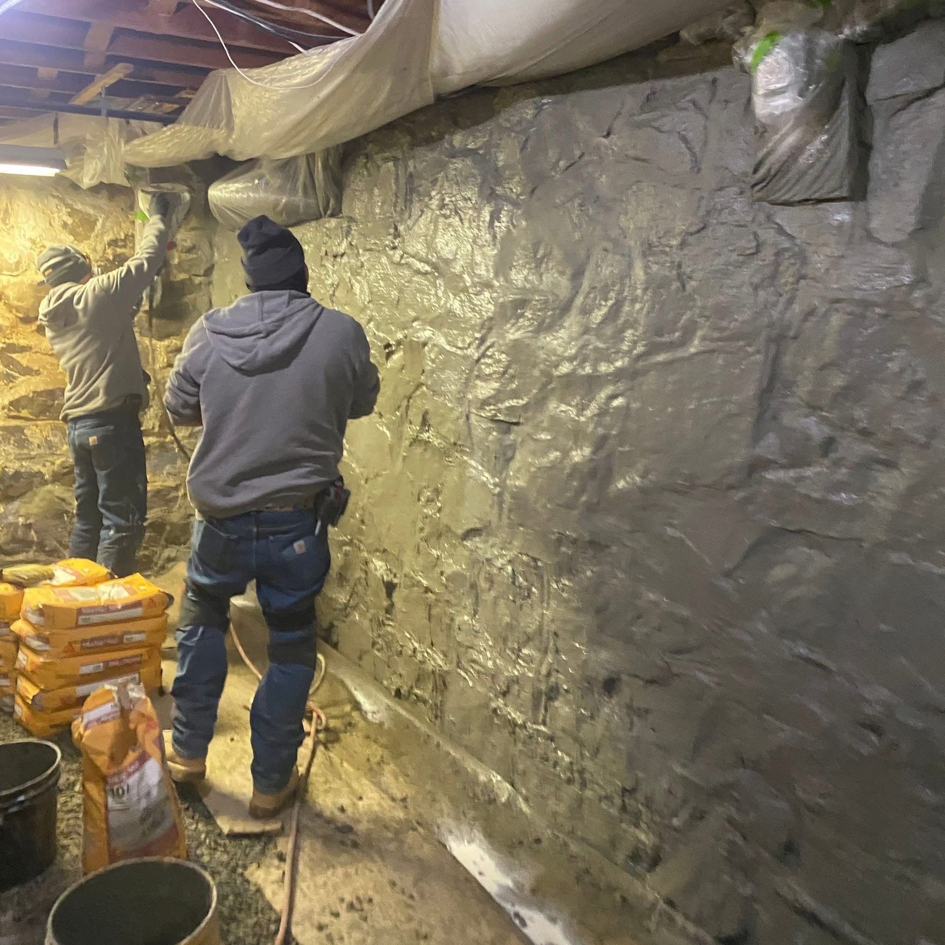 Two men are working on a wall in a basement