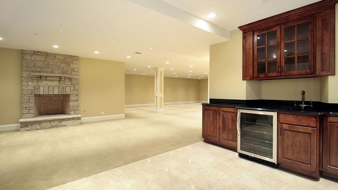 An empty basement with a fireplace and a refrigerator