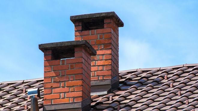 Two brick chimneys are sitting on top of a tiled roof.