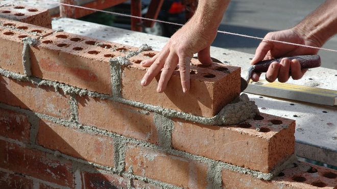 A person is laying bricks on a wall with a trowel.