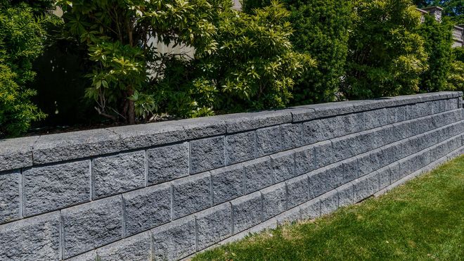 A brick wall is surrounded by trees and grass in a yard.