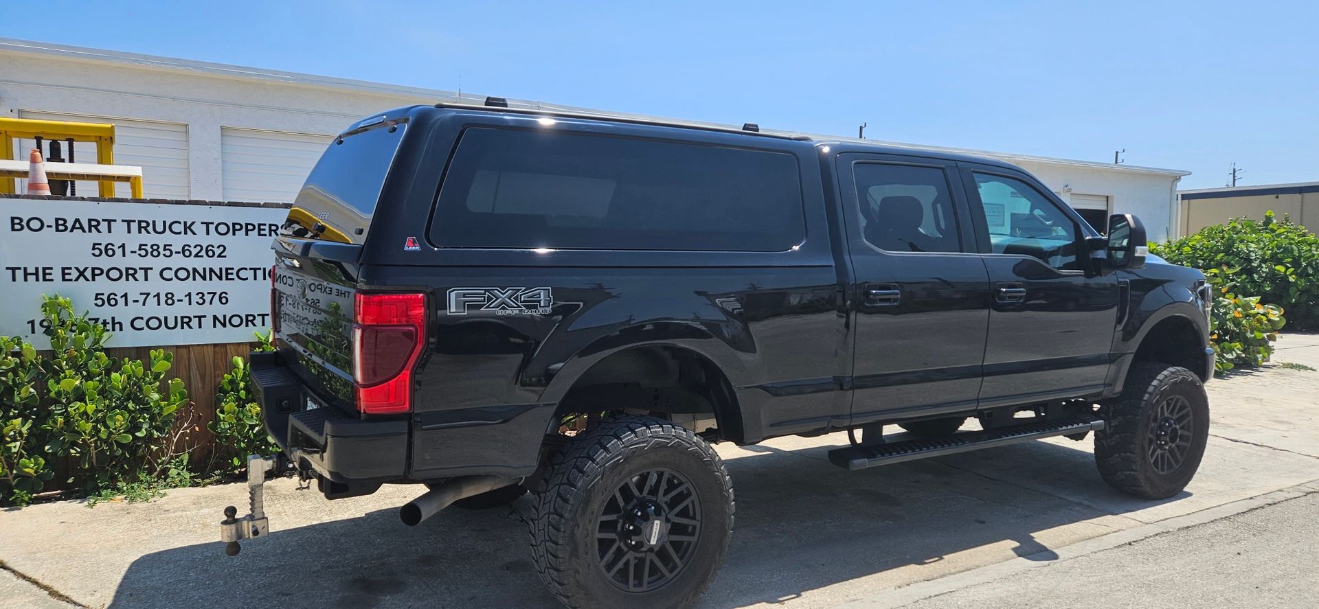 Black lifted pickup truck parked beside a roadside sign in a sunny outdoor area