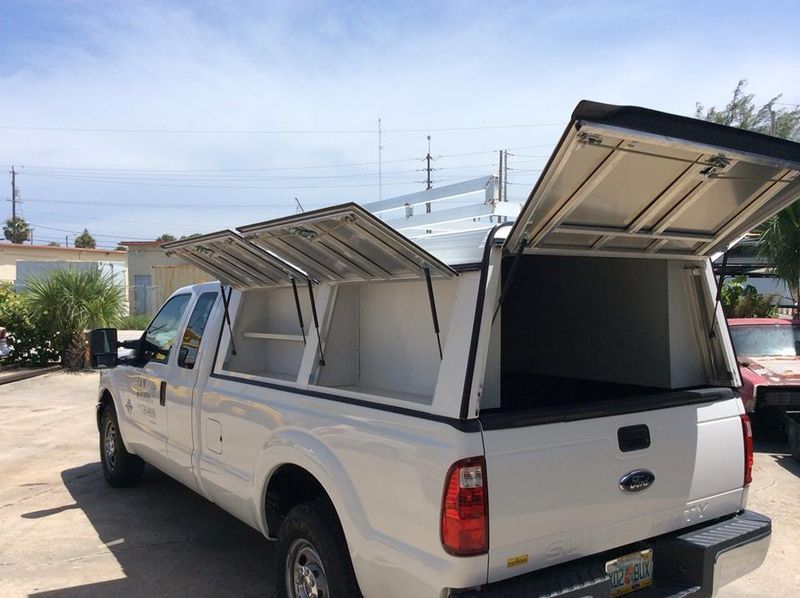 White pickup truck with open canopy compartments parked outdoors on a sunny street