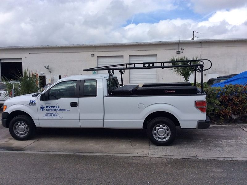 White pickup truck with roof rack parked beside a building under cloudy skies