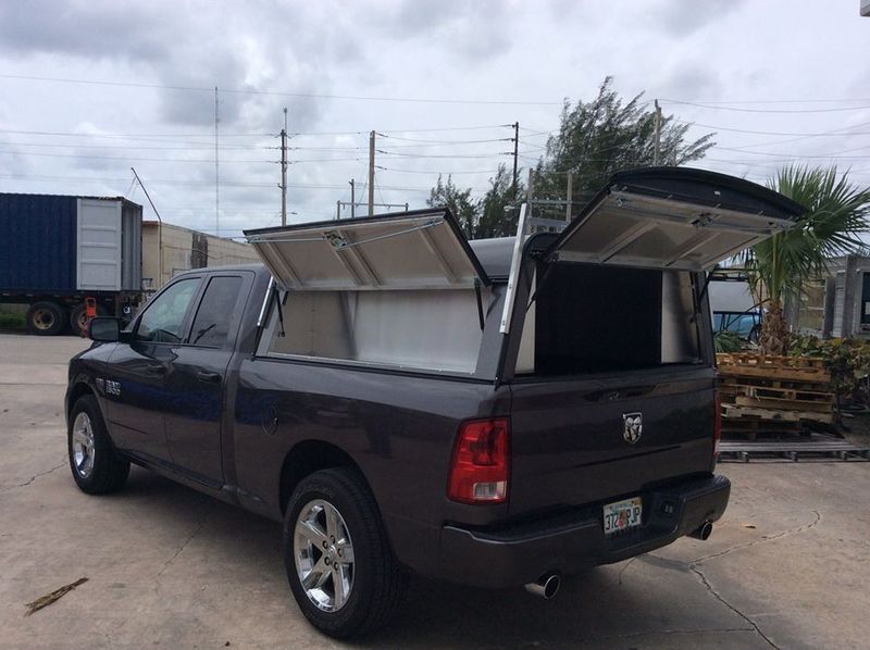 Dark pickup truck with open utility compartments parked outdoors on a cloudy day