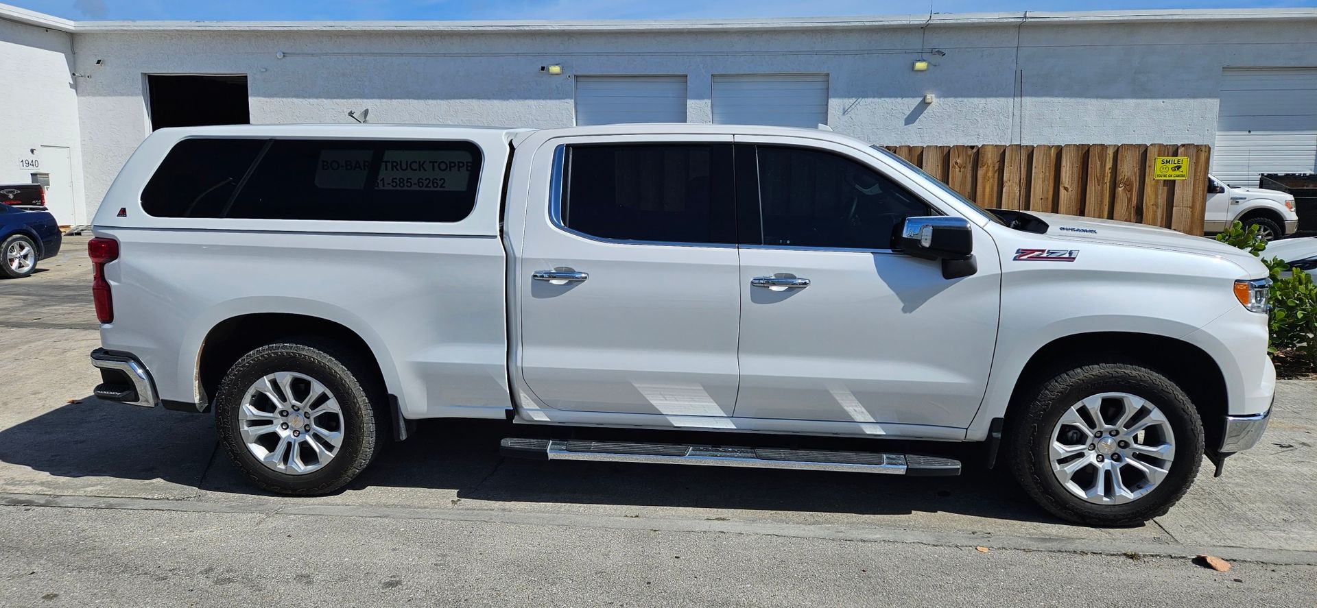 White pickup truck with camper shell parked beside a building on a street.