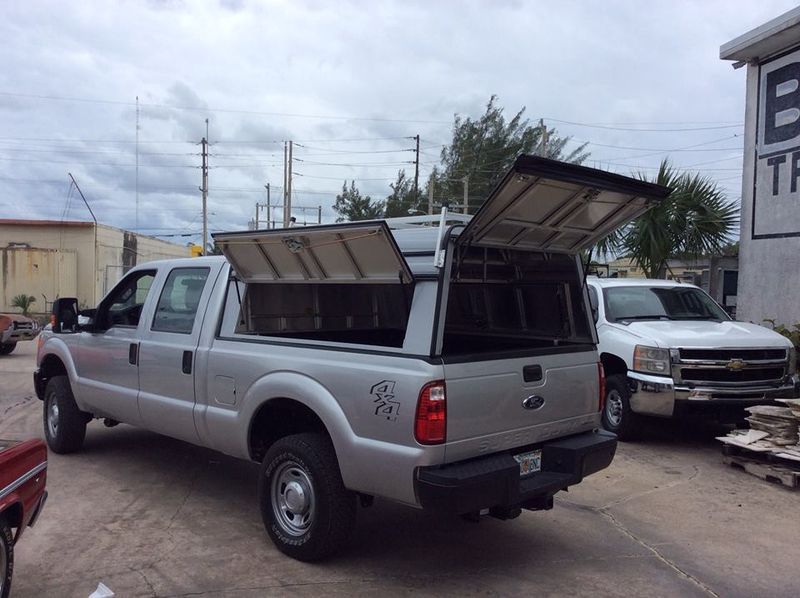 Silver pickup truck with open camper shell compartments in an outdoor lot